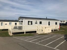 A fenced raised mobile home with a small table and chairs beside a parking lot at No30 Elm Rise in Gristhorpe near Filey
