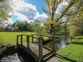 An outdoor area with a bridge over a pond and a cottage in the background at Pultheley Cottage near Hyssington