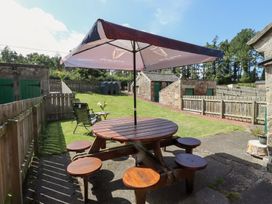 A garden with a wooden table and chairs under an umbrella at Kits Cottage Middleton near Belford
