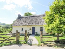 A thatched cottage with a wooden gate and gravel path leading to a blue door surrounded by grass and trees at Thatched Cottage in Llanybydder