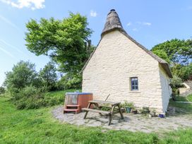 A stone cottage with a thatched roof a wooden picnic table and a hot tub in a garden at Thatched Cottage in Llanybydder