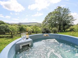 An outdoor hot tub with two wine glasses and a bottle of wine with trees and hills in the background at Thatched Cottage in Llanybydder