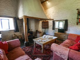 A living room with stone walls a wood burning stove wooden table two sofas and a television at Thatched Cottage in Llanybydder
