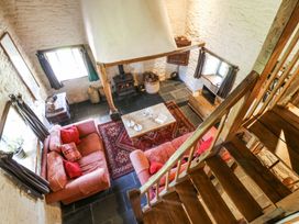 A living room with two sofas around a coffee table and wood stove with stone walls at Thatched Cottage in Llanybydder