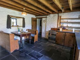 A kitchen with wooden beams stone walls built in wooden benches table stove and shelves with dishes at Thatched Cottage in Llanybydder