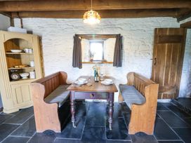 A dining area with wooden benches a table set with dishes and wine glasses a cabinet and a small window at Thatched Cottage in Llanybydder