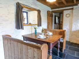 A dining area with a wooden table and bench seats set for two in a room with white stone walls and a small window at Thatched Cottage in Llanybydder