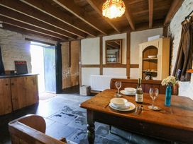 A dining area with wooden table set with plates wine glasses and a bottle next to a cabinet and stone walls at Thatched Cottage in Llanybydder