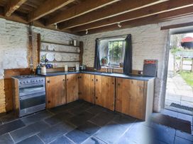 A kitchen with wooden cabinets stone walls open shelves and a stove at Thatched Cottage in Llanybydder