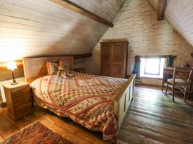 A bedroom with wooden furniture a quilted bedspread a teddy bear a desk and a window at Thatched Cottage in Llanybydder