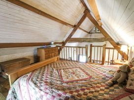 A loft bedroom with a bed and teddy bear a wooden chest and dresser with rustic beams at Thatched Cottage in Llanybydder