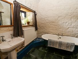 A bathroom with a bathtub a sink a mirror a radiator a small window with curtains and a plant at Thatched Cottage Llanybydder
