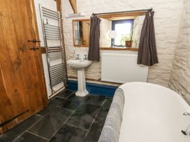 A bathroom with a white pedestal sink a bathtub a wooden door a window with curtains and a plant and a heated towel rail at Thatched Cottage Llanybydder