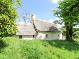 A thatched roof stone cottage surrounded by grass and trees at Thatched Cottage in Llanybydder