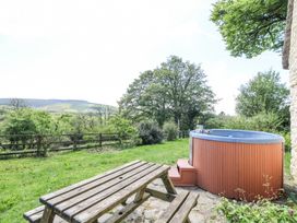 An outdoor area with a wooden picnic table and a hot tub next to a stone building at Thatched Cottage in Llanybydder