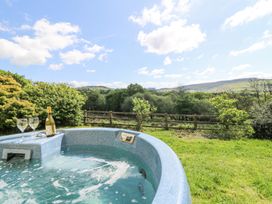 An outdoor hot tub with two wine glasses and a bottle overlooking a grassy garden and hills at Thatched Cottage in Llanybydder