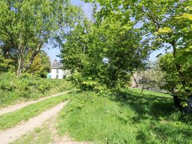 A dirt path with trees and grass leading to a white house with a thatched roof at Thatched Cottage in Llanybydder
