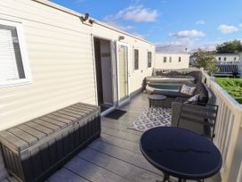 An outdoor deck with a round table black storage box sofa and hot tub at HD Retreat in Tattershall