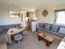 A living area with gray sofas, round stools, a wooden table, and a kitchen area at HD Retreat in Tattershall