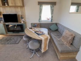 A living area with a grey corner sofa a wooden dining table with two stools a TV mounted on a wooden cabinet and a window with curtains at HD Retreat in Tattershall