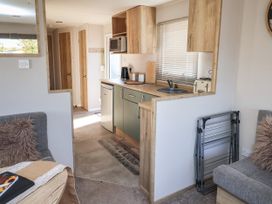 A kitchen with wooden cabinets a sink toaster and microwave visible from a living room with grey seating and a folding drying rack at HD Retreat in Tattershall