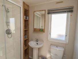 A bathroom with a shower, wooden shelves, a sink with a mirror above it, a window with blinds, and a toilet at HD Retreat in Tattershall
