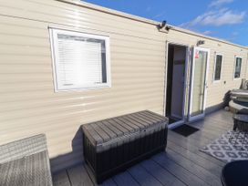 An exterior view of a beige mobile home with a window a black storage box an open door and outdoor seating at HD Retreat in Tattershall