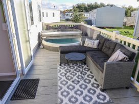An outdoor deck with a sectional sofa a small round table a rug and a hot tub at HD Retreat in Tattershall