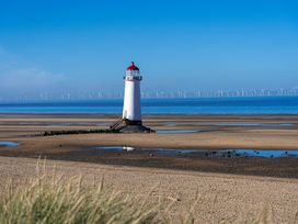 A lighthouse on a sandy beach with wind turbines in the sea at Rivendell in Ffynnongroyw