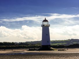 A lighthouse on a sandy beach with hills and vegetation in the background at Rivendell in Ffynnongroyw