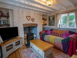 A living room with a patterned sofa and cushions a wooden coffee table a TV on a stand a fireplace with firewood and hanging hearts and a window with curtains at Rivendell in Ffynnongroyw