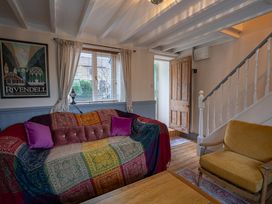 A living room with a sofa covered by a colorful throw and purple cushions a yellow armchair a wooden door and stairs at Rivendell in Ffynnongroyw