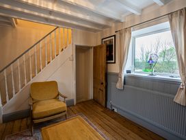 A room with a wooden floor a mustard yellow chair a wooden coffee table stairs with white railings a wooden door a window with curtains and a blue lamp on the sill at Rivendell in Ffynnongroyw