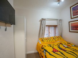 A bedroom with a bed covered in yellow patterned bedding a white wardrobe a wall-mounted TV and framed pictures at Rivendell in Ffynnongroyw