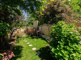 A garden with bushes grass stepping stones and a wooden deck with a barbecue at Rivendell in Ffynnongroyw