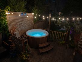 An outdoor wooden deck with a round hot tub illuminated in blue string lights and plants at Rivendell in Ffynnongroyw
