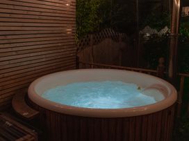 An outdoor hot tub with water lit up at night surrounded by wooden fencing and greenery at Rivendell in Ffynnongroyw
