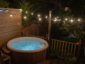 An outdoor hot tub with bubbling water and string lights in a garden at Rivendell in Ffynnongroyw