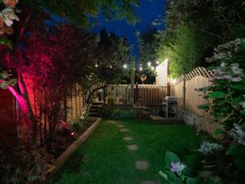 A garden with grass a wooden fence string lights and a barbecue grill at Rivendell in Ffynnongroyw