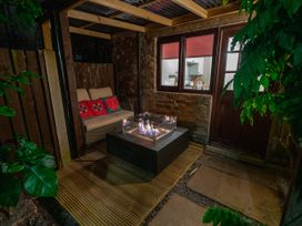 An outdoor seating area with a sofa red cushions and a fire pit next to a stone wall and door at Rivendell in Ffynnongroyw