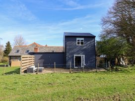A fenced patio with outdoor seating and a two-story house with a slate roof and wooden walls at The Stables in Tafarn-Y-Gelyn