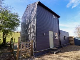 An exterior view of a dark grey metal sided building with a small beige door and steps surrounded by a wooden gate and gravel at The Stables in Tafarn-Y-Gelyn