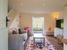 A living room with a sofa a chair a coffee table a television and an open door showing a grassy field at The Stables in Tafarn-Y-Gelyn