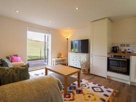 A living room with a couch a wooden coffee table a colorful rug a TV on a cabinet a floor lamp and a kitchen area at The Stables in Tafarn-Y-Gelyn