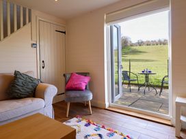 A sitting area with a sofa and chair next to a door opening to a patio with a table and two chairs overlooking a grassy field at The Stables in Tafarn-Y-Gelyn