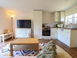 A living room with a TV, wooden coffee table, floor lamp and an open kitchen area at The Stables in Tafarn-Y-Gelyn