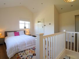 A bedroom with a bed and nightstands next to a window and white wooden railing at The Stables in Tafarn-Y-Gelyn