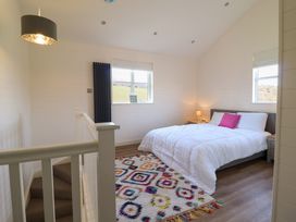 A bedroom with a bed with white bedding and a pink pillow a colorful rug two windows and a staircase with white railings at The Stables in Tafarn-Y-Gelyn