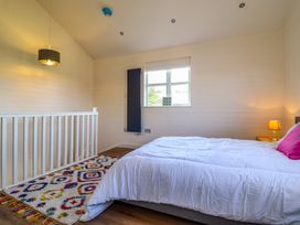 A bedroom with a bed white bedding pink pillow a colorful rug window and a lamp at The Stables in Tafarn-Y-Gelyn