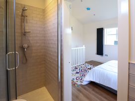 A bathroom with a glass shower door leading to a bedroom with a bed a colorful rug and a window at The Stables in Tafarn-Y-Gelyn